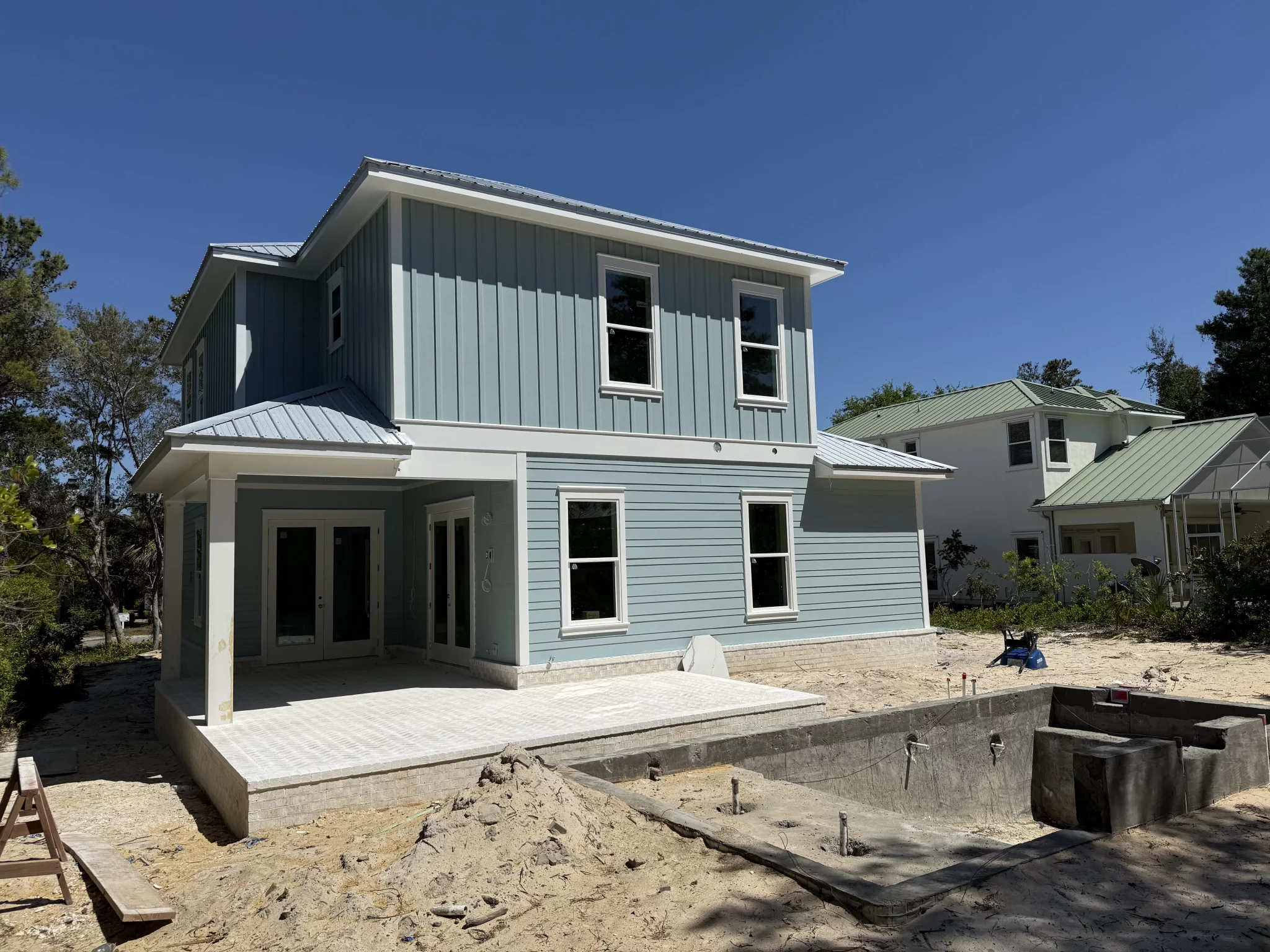 New construction two-story light blue house with white trim and a pool under construction.